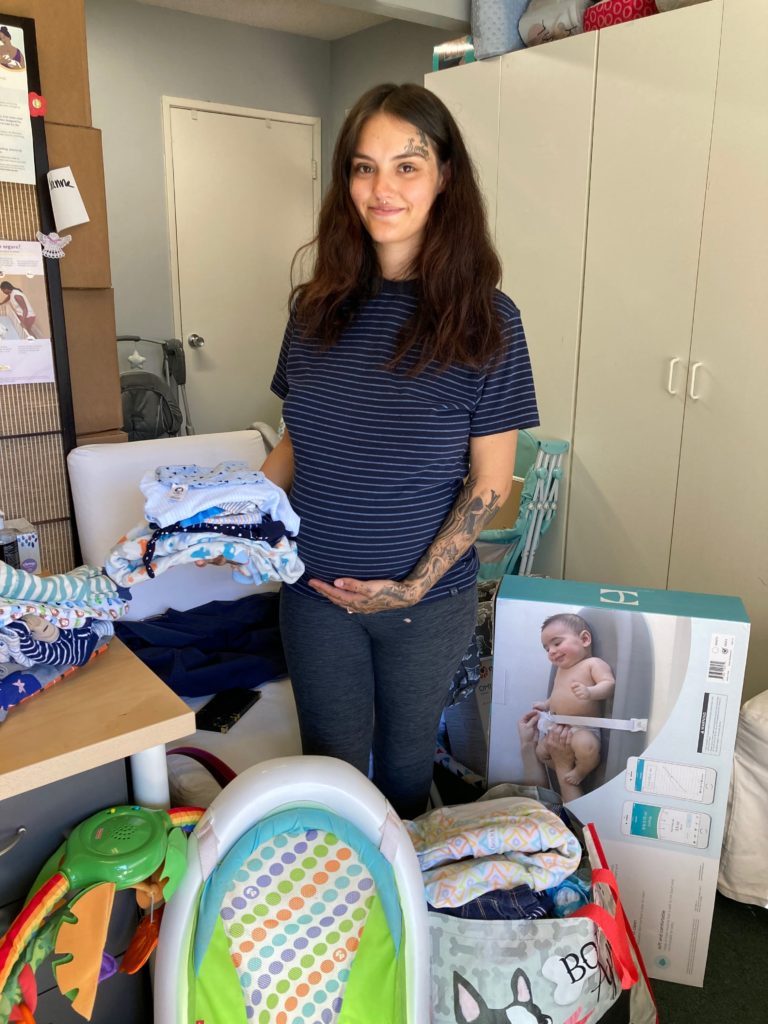 woman holding children's clothes and standing amongst child supplies